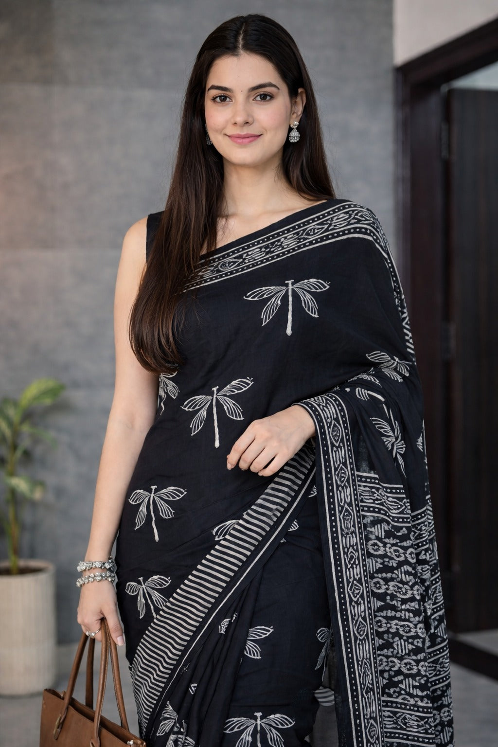 Woman wearing a black saree with white patterns, standing indoors.