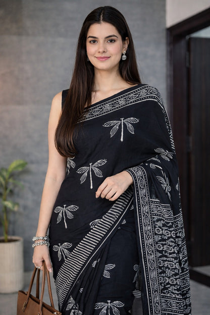 Woman wearing a black saree with white patterns, standing indoors.