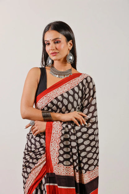 Black cotton saree with ivory leaf block print and handcrafted red border – close-up drape.